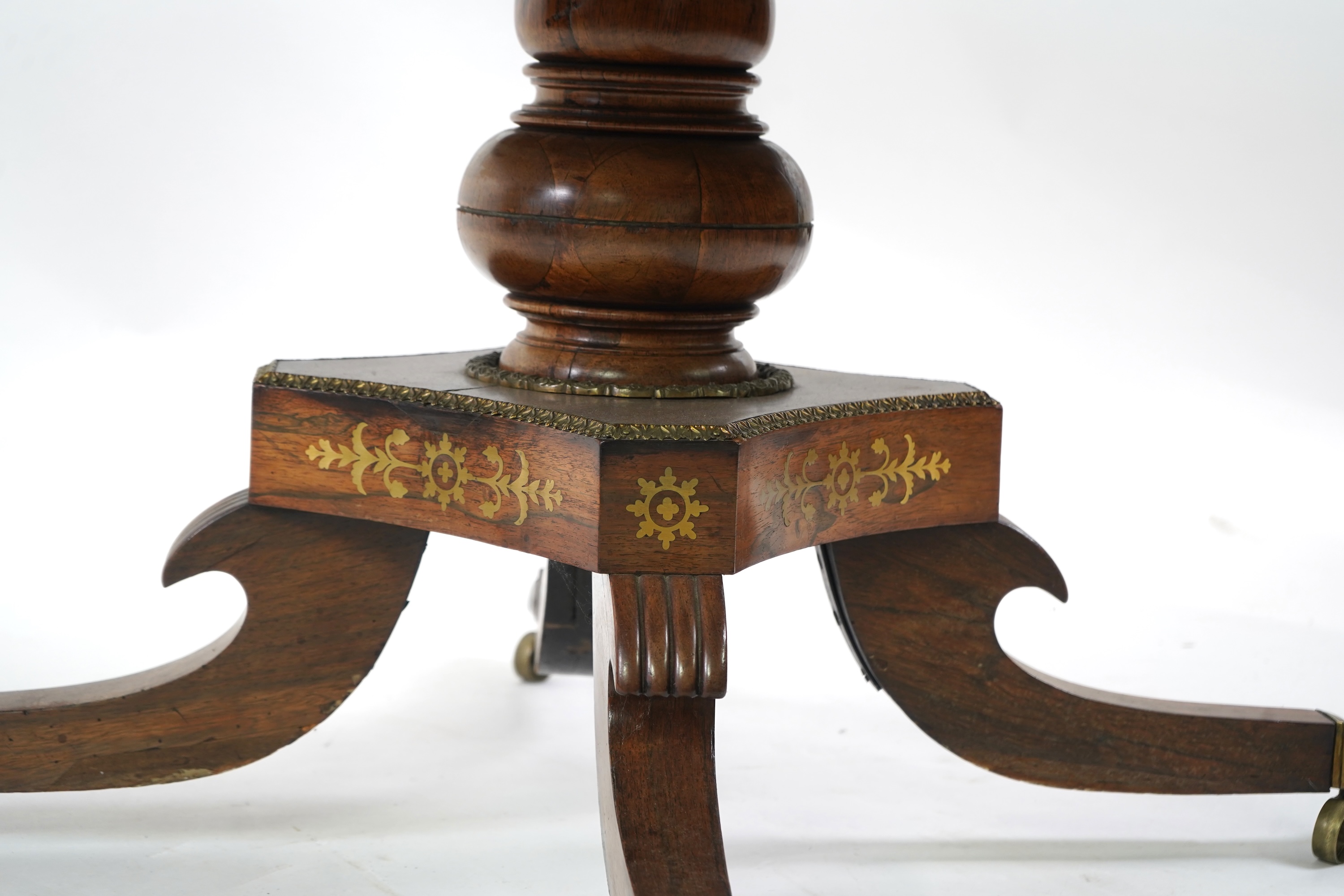 A Regency cut brass inlaid and gilt metal mounted circular rosewood breakfast table, the bird's-eye maple banded tilt top on baluster column, concave platform and quadruple downswept base with cast claw caps and castors,